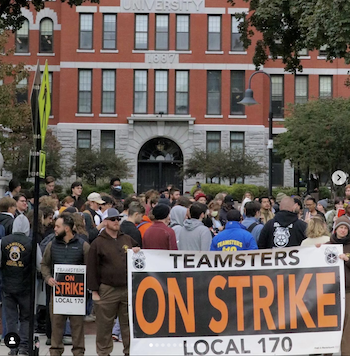 Grad students at Clark University hold a banner in front of an administration building. The banner reads "Teamsters on strike, Local 170"